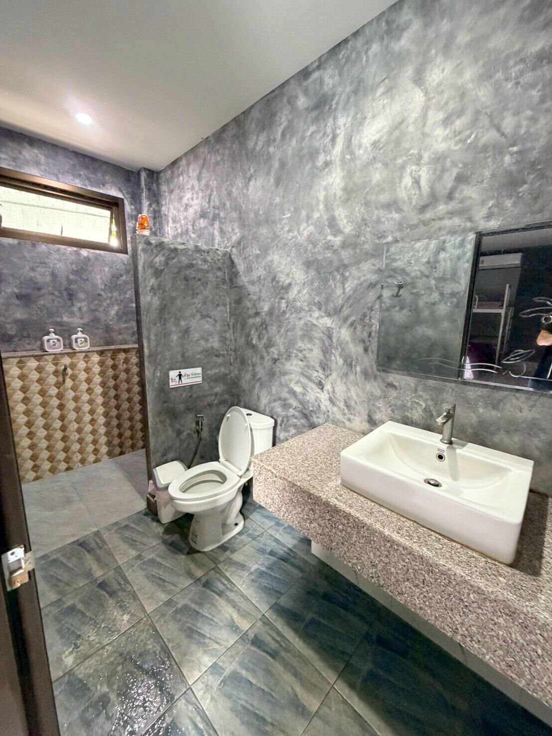 Ein Badezimmer mit einer weißen Toilette, einem Waschbecken und einer Wand mit Struktur.