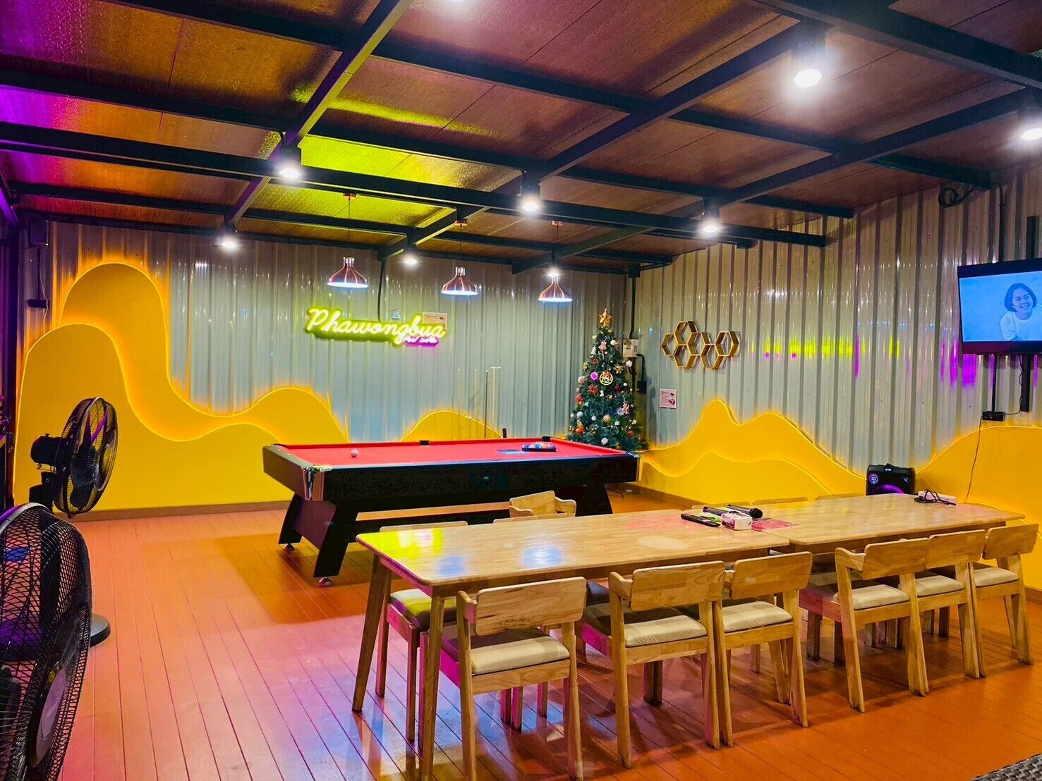 A billiards room with a pool table, chairs, a Christmas tree, and a neon sign.