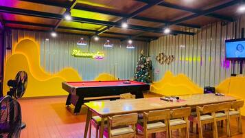 A billiards room with a pool table, chairs, a Christmas tree, and a neon sign.