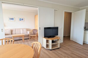 Ein modernes Wohnzimmer mit einer Couch, Sesseln, einem Fernseher und einem Esstisch.