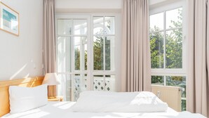 Ein Hotelzimmer mit Bett, Nachttisch, Lampe und einem Fenster mit Vorhängen.