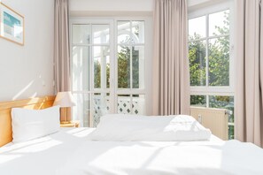 Ein Hotelzimmer mit Bett, Nachttisch, Lampe und einem Fenster mit Vorhängen.