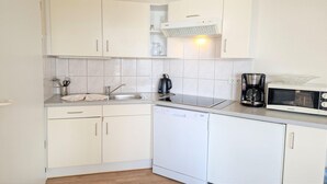 Eine kompakte Küche mit weißen Schränken, einem Geschirrspüler, einer Kaffeemaschine und einer Mikrowelle.