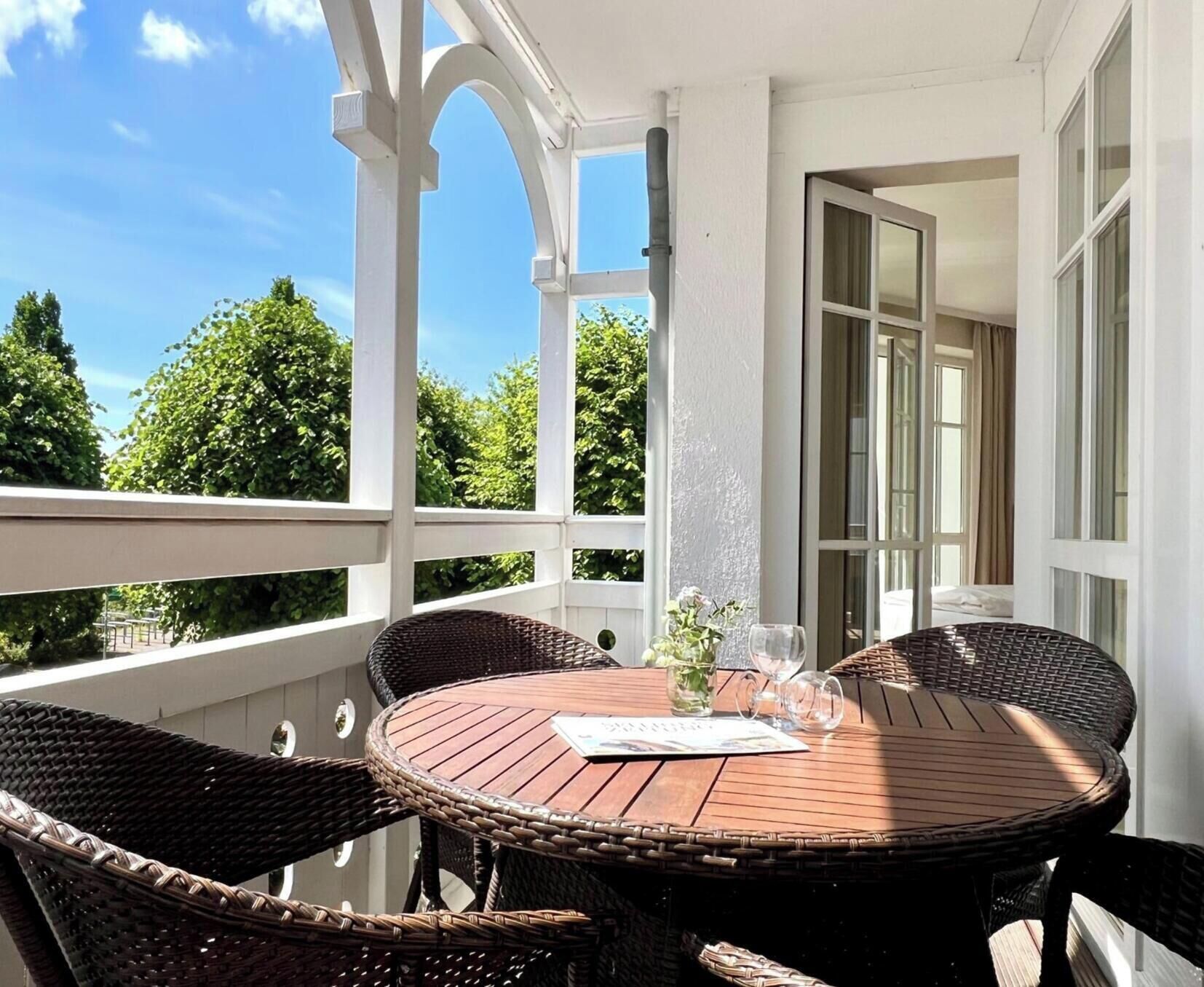 A balcony with a round wooden table, wicker chairs, and a potted plant.