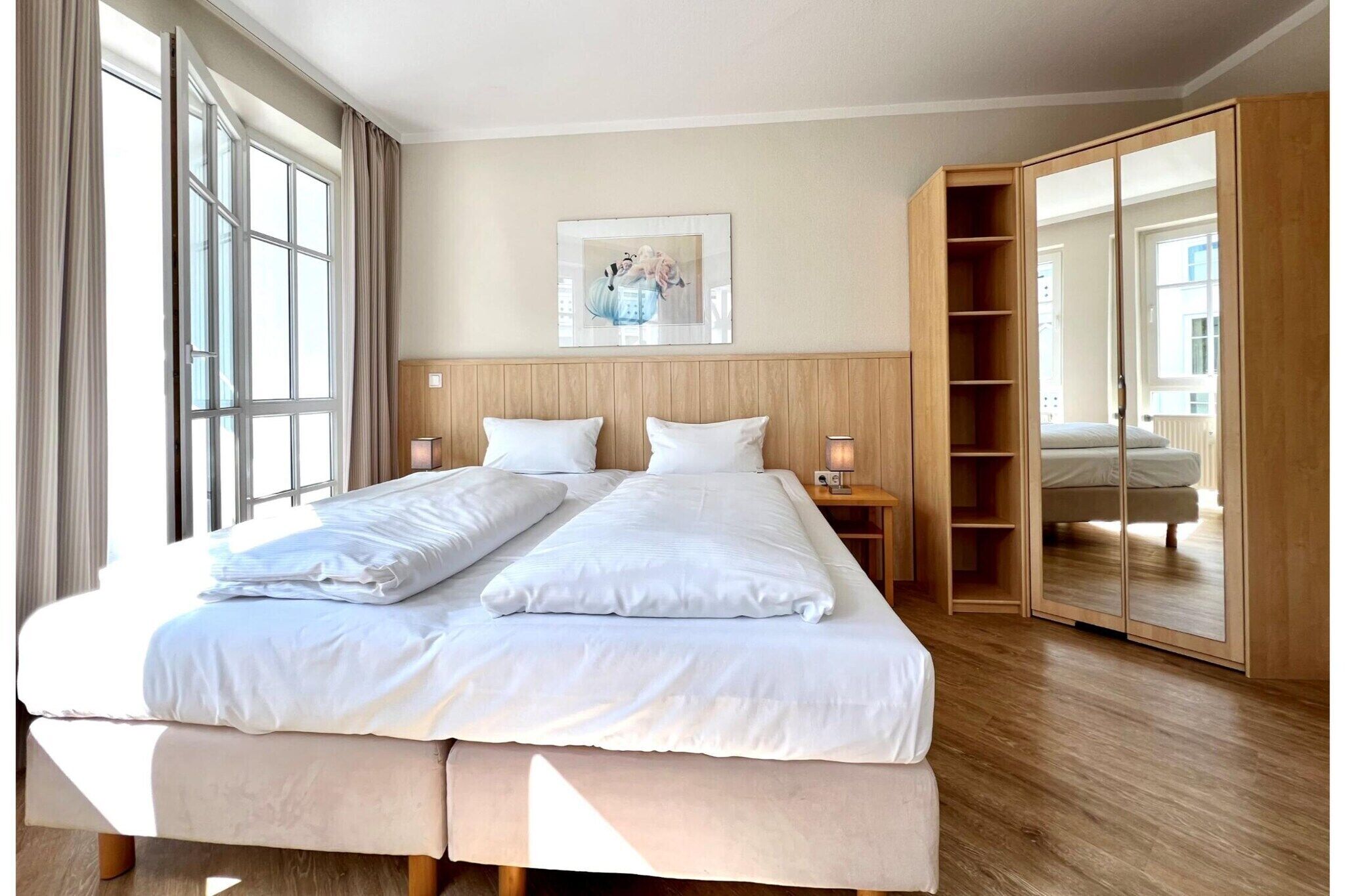 Una cama doble con ropa de cama blanca, un cabecero de madera, una mesita de noche con lámpara y un armario grande con puertas espejadas.