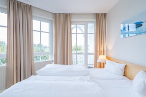 Habitación de hotel con cama, cortinas, una ventana y un cuadro en la pared.