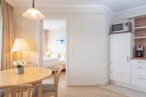 Habitación de hotel con comedor, cama, kitchenette y baño visible a través de una puerta abierta.