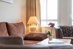 Una sala de estar con un sofá, una lámpara, una mesa con una planta y una ventana con cortinas.