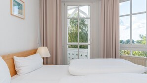 Habitación de hotel con cama, lámpara, ventana con cortinas y vistas a zonas verdes.