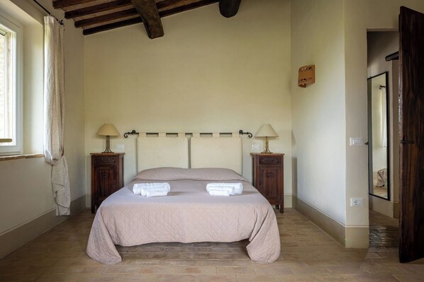 A bedroom with a bed, two bedside tables, a window, and a door.