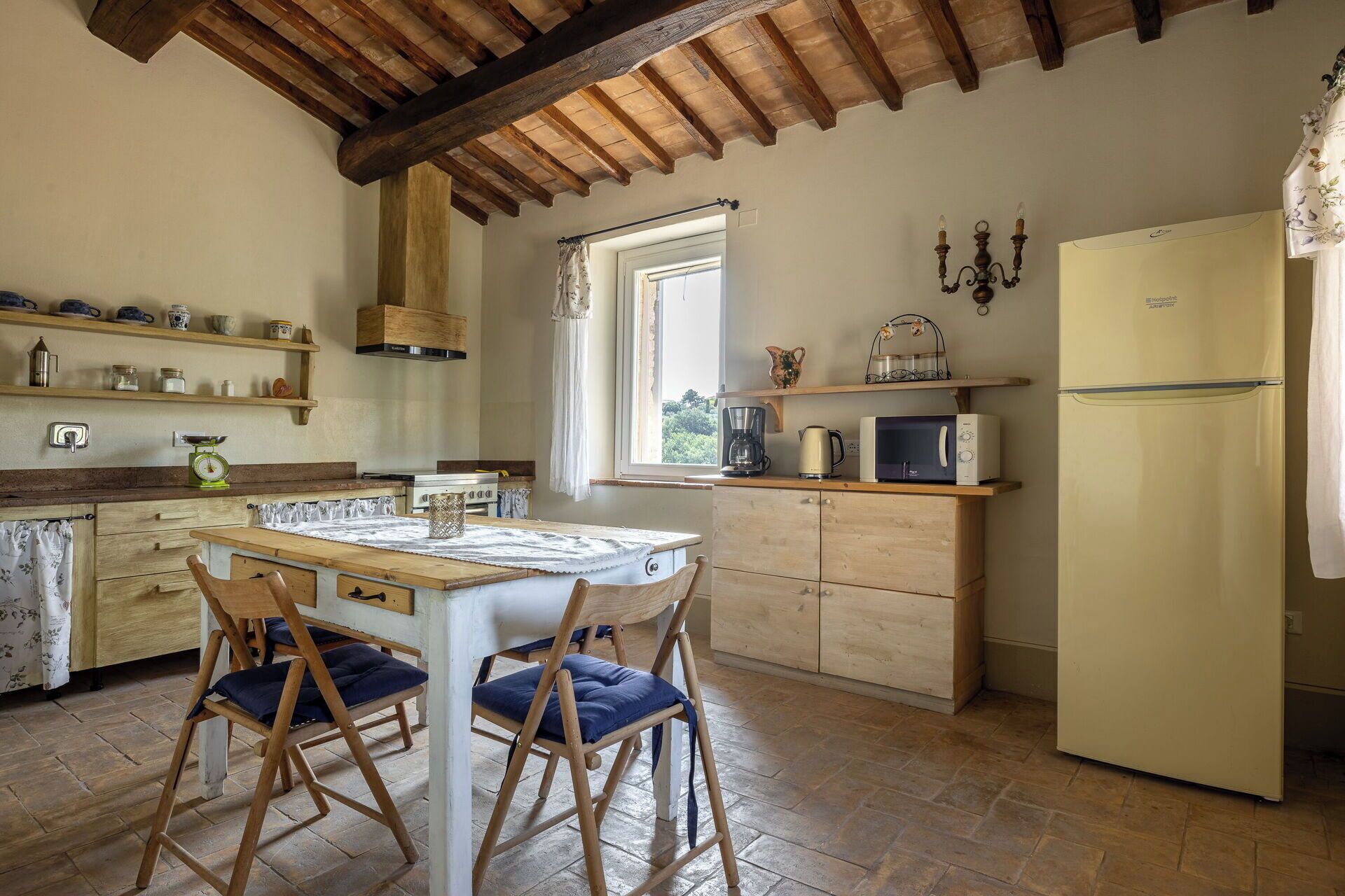 Une cuisine avec des meubles en bois, une table à manger avec des chaises, un réfrigérateur et une fenêtre qui laisse entrer la lumière naturelle.