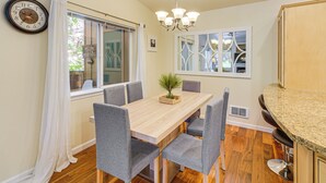 A dining area with a wooden table, grey chairs, a chandelier, and a window with a view of trees. - Quiet Condo Next to Enchantment, Adventure Parks (Leavenworth)
