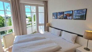 A hotel room with a large bed, two bedside tables, a window with curtains, and three framed pictures on the wall. - Komforturlaub auf Rügen (Sellin)