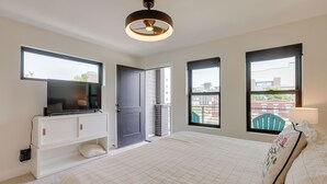 Ein Schlafzimmer mit einem Bett, einem Fernseher auf einer weißen Kommode, einem Deckenventilator und großen Fenstern.