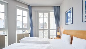 Hotellihuone, jossa on kaksi sänkyä, puinen pääty, ikkuna verhoilla ja seinällä oleva kehystetty taulu.