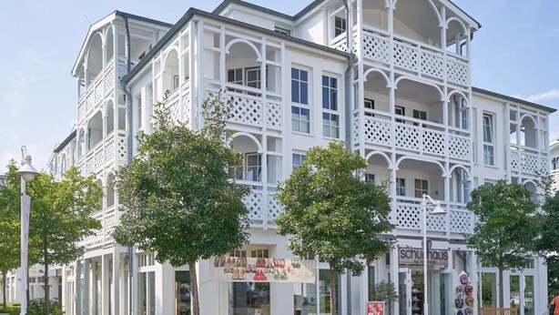 A white building with multiple balconies and a storefront with a sign. - Ferienwohnung im 2.OG mit Balkon in Sellin (Sellin)