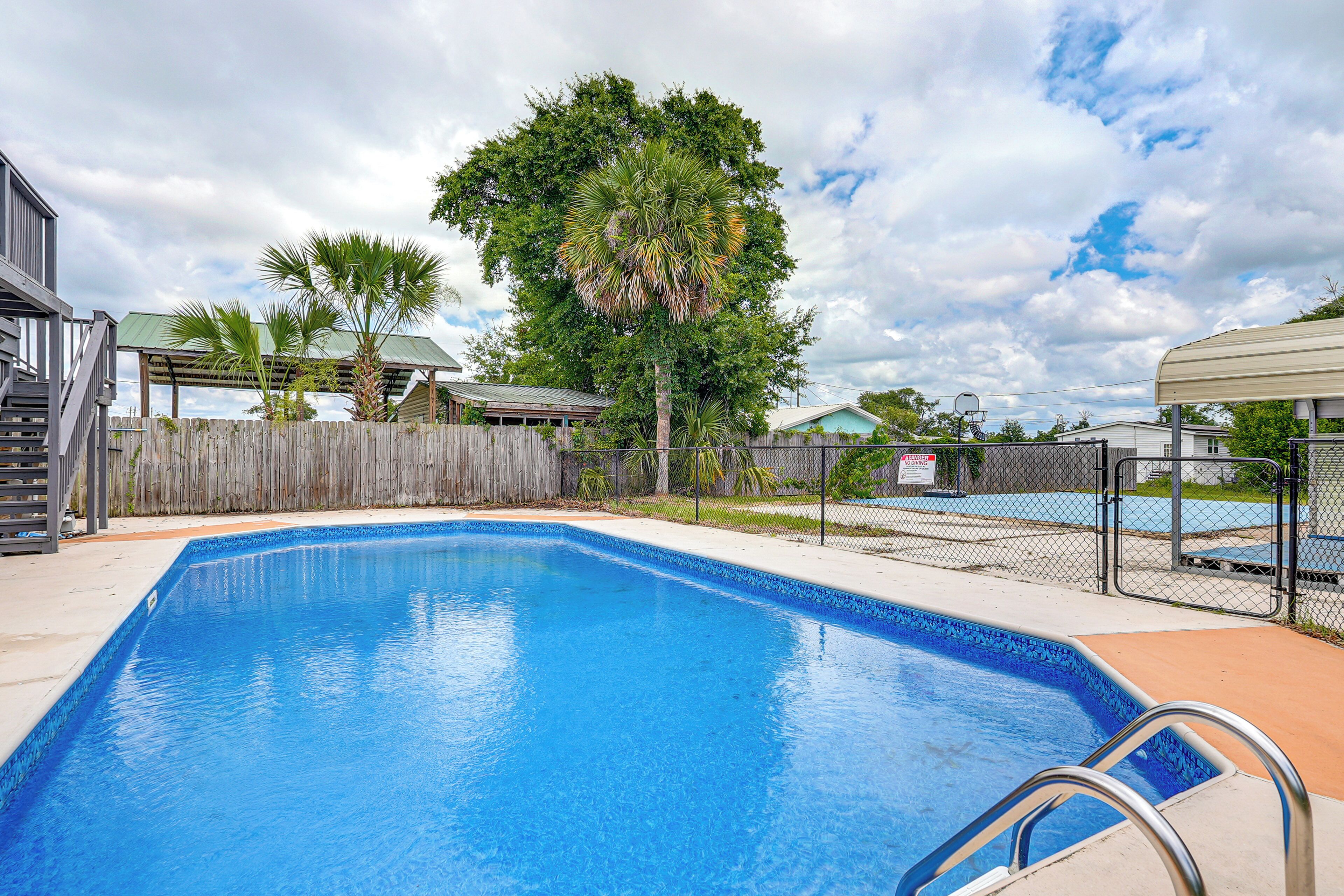 A swimming pool with a metal ladder, surrounded by a wooden fence and palm trees.