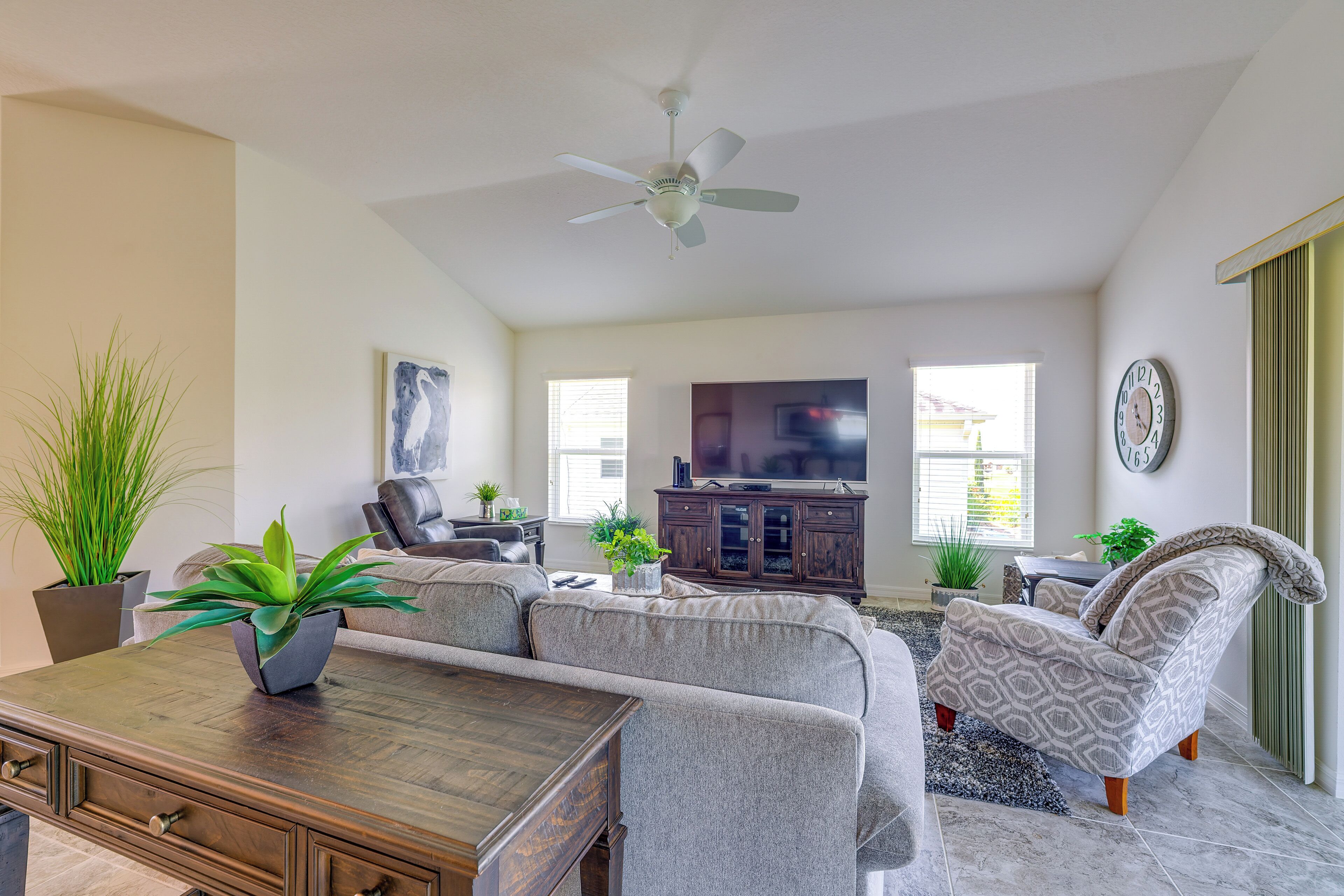 A living room with a sofa, armchair, coffee table, TV, and ceiling fan.