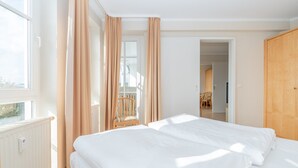 Une chambre à coucher avec un lit, des rideaux, une chaise et une vue sur l’extérieur.