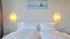Une chambre d’hôtel avec un lit, deux lampes de chevet et un tableau représentant des voiliers accroché au mur.