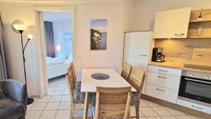 Une cuisine moderne avec des meubles blancs, un four encastré et un coin repas comprenant une table et des chaises.