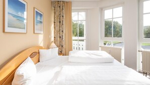 Ein Hotelzimmer mit einem großen Bett, zwei gerahmten Bildern an der Wand, einem Fenster mit Blick auf Grünflächen und einer Tür, die zu einem Außenbereich führt.