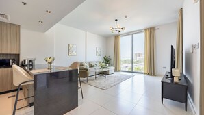 Un salon moderne comprenant un canapé, une table basse, un téléviseur et un coin cuisine équipé d’un four à micro-ondes et d’une bouilloire.