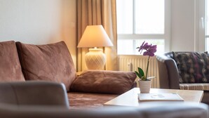 Un salon avec un canapé, une lampe, une table avec une plante et une fenêtre avec des rideaux.