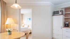 Une chambre d’hôtel comprenant un coin repas, un lit, une kitchenette et une salle de bain, le tout visible à travers une porte ouverte.