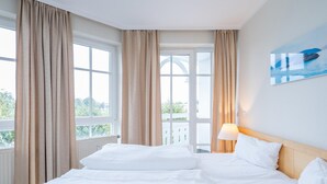 Une chambre d’hôtel avec un lit, des rideaux, une fenêtre et un tableau au mur.