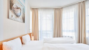 Ein Hotelzimmer mit einem großen Bett, einem Nachttisch, einer Lampe, einem Bild an der Wand und einem Fenster mit Vorhängen.