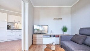 A modern living room with a grey sofa, a wooden coffee table, a TV on a white cabinet, and a kitchen in the background. - Ferienwohnung mit ausreichend Platz in Sellin (Sellin)