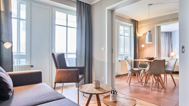 A modern hotel room with a sofa, chairs, a dining table, and a lamp. - Ferienwohnung mit ausreichend Platz in Sellin (Sellin)
