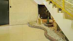 Una escalera con barandilla amarilla, un muro de ladrillo y un pequeño jardín con un cactus y piedras decorativas.
