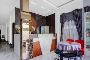 A hotel reception area with a marble counter, a refrigerator, a dining area with a table and chairs, and a glass cabinet with items. - Heritage Stay Near Al-Mashun Mosque (Medan)