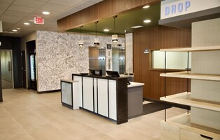 A hotel reception area with a modern design, including a reception desk, a 'DROP' sign, and an elevator.
