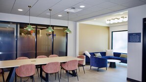 Een moderne vergaderruimte met een lange tafel, verschillende stoelen, een blauwe bank en een wandgemonteerd scherm.