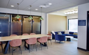 A modern meeting room with a long table, several chairs, a blue sofa, and a wall-mounted screen. - Livsmart Studios BY Hilton Clarksville (Clarksville)