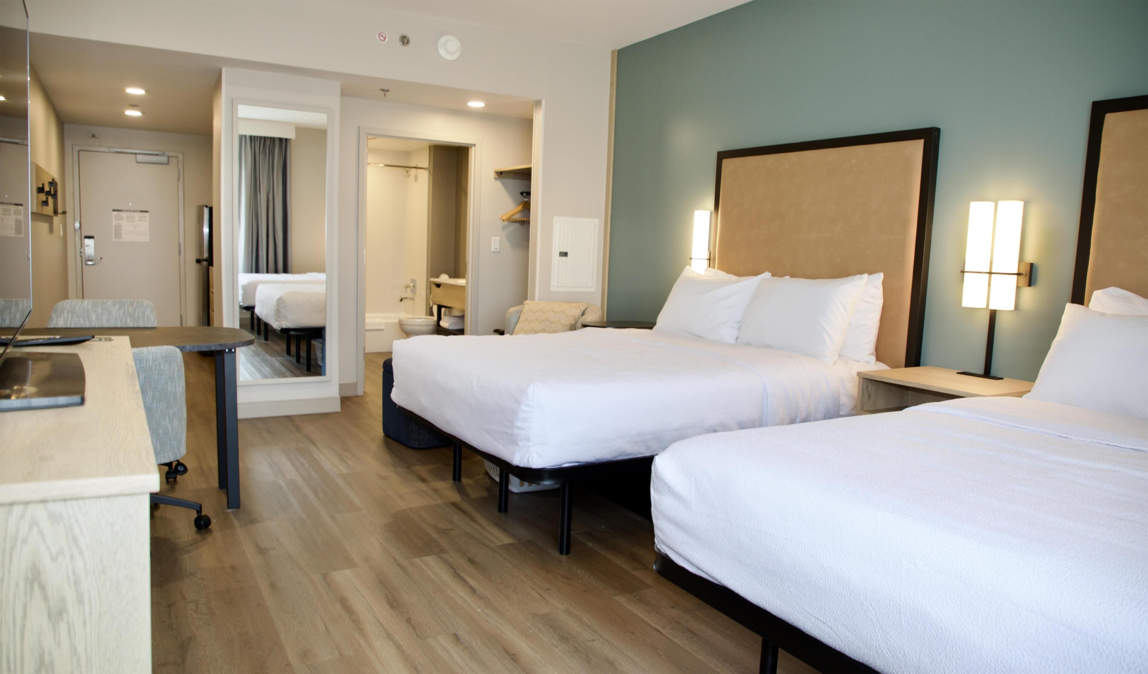 A hotel room with two beds, a desk, a chair, a bathroom, and a shower area.