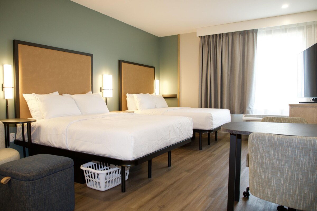 Habitación de hotel con dos camas, un escritorio, una silla, un televisor y una ventana con cortinas.