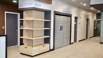 A hallway with a 'DELIVERY DROP' sign, a fire alarm, and a set of lockers.
