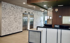 A hotel reception area with a wall decorated with doodles, two elevators, and a sign indicating the manager's office. - Livsmart Studios BY Hilton Clarksville (Clarksville)
