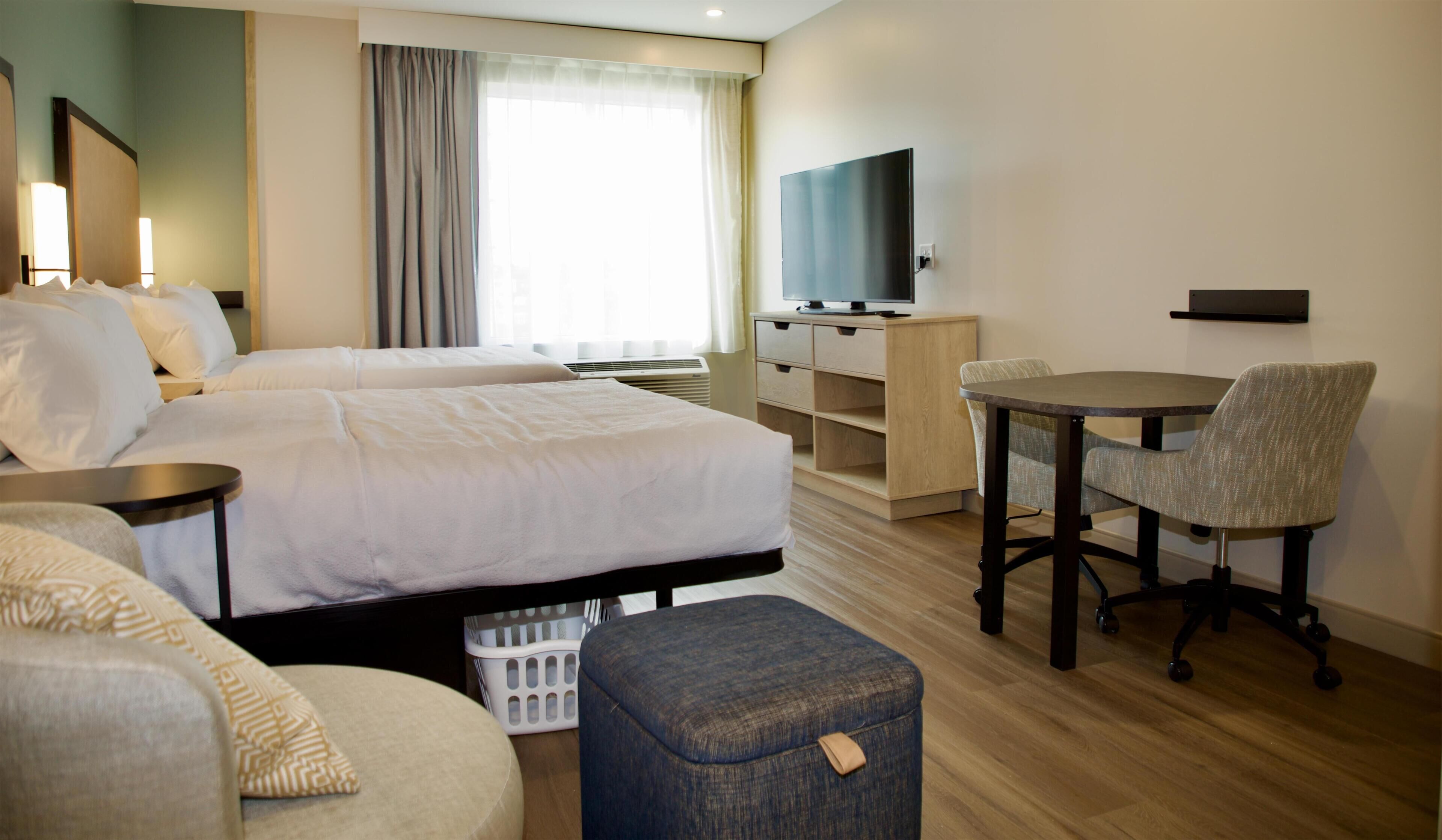 Una habitación de hotel con dos camas, un escritorio, una silla, un televisor y una mesita.