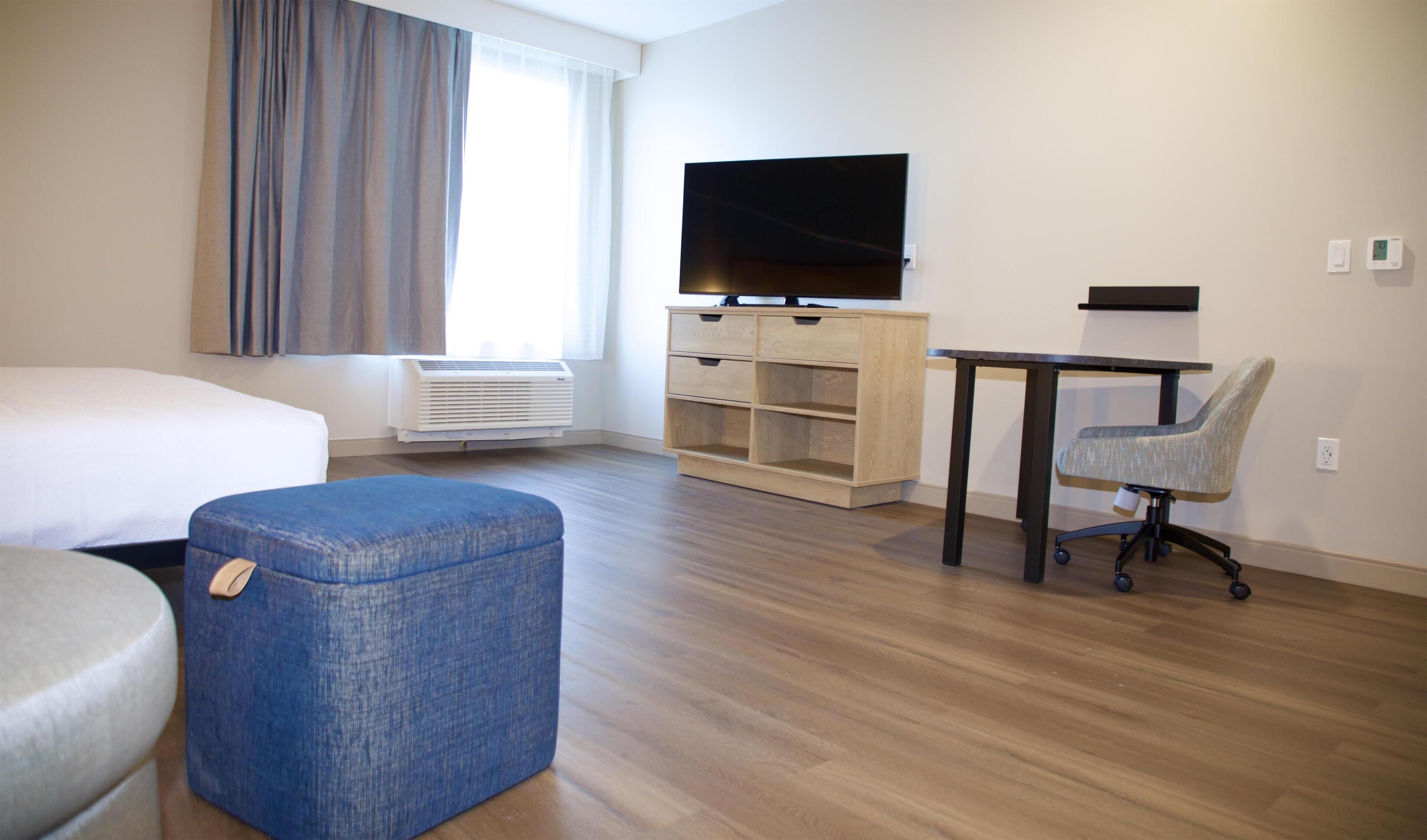 A hotel room with a bed, a desk, a chair, a television, and a window with curtains.