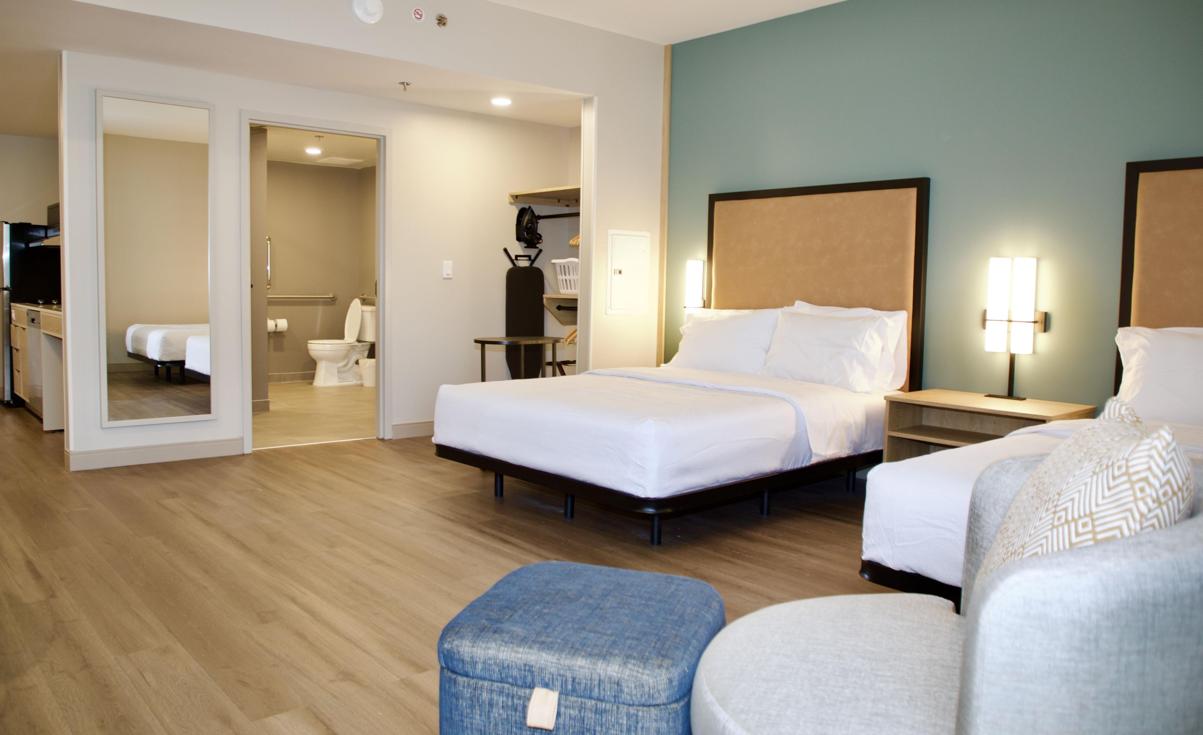 A hotel room with a large bed, a smaller bed, a desk, a chair, and a bathroom visible through an open door.