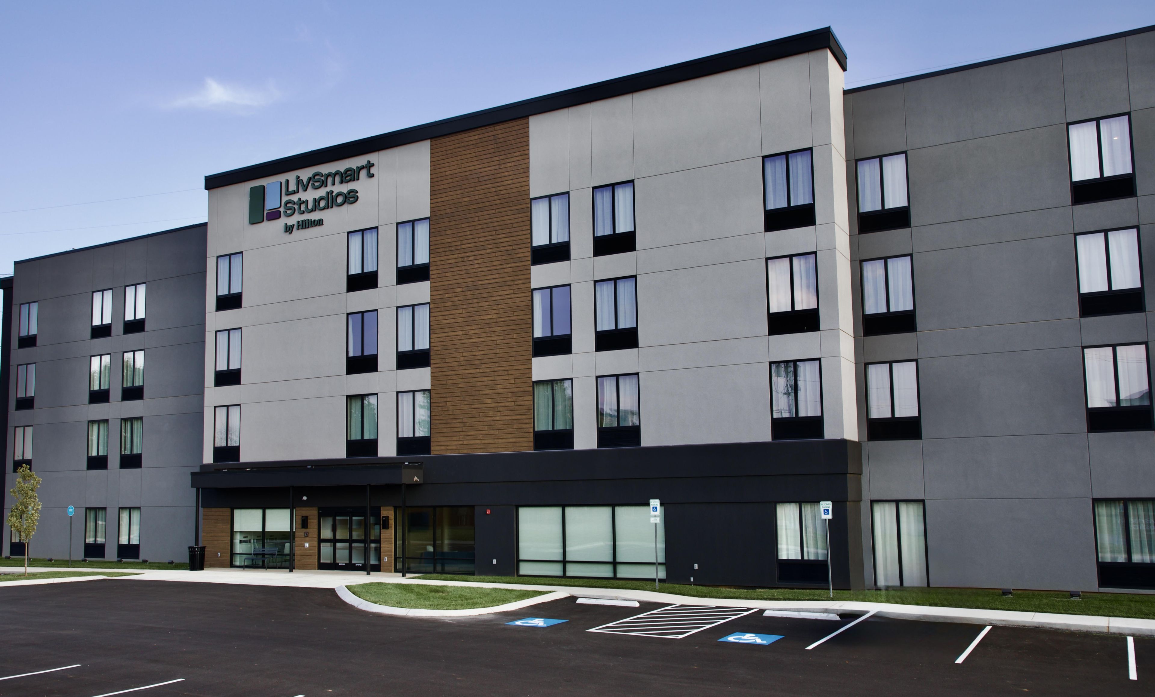 A modern hotel building with a sign for 'LIVSmart Studios by Hilton' and a parking lot with handicapped parking spaces.