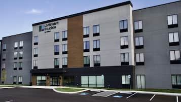 En modern hotellbyggnad med en skylt som visar texten ”LIVSmart Studios by Hilton” och en parkeringsplats med parkeringsplatser reserverade för personer med funktionsnedsättning.