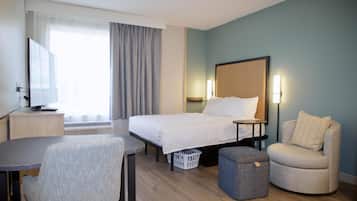 A hotel room with a bed, a desk, a chair, a TV, and a window with curtains.
