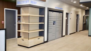Een gang met een 'DELIVERY DROP' bord, een rookmelder en een rij lockers.