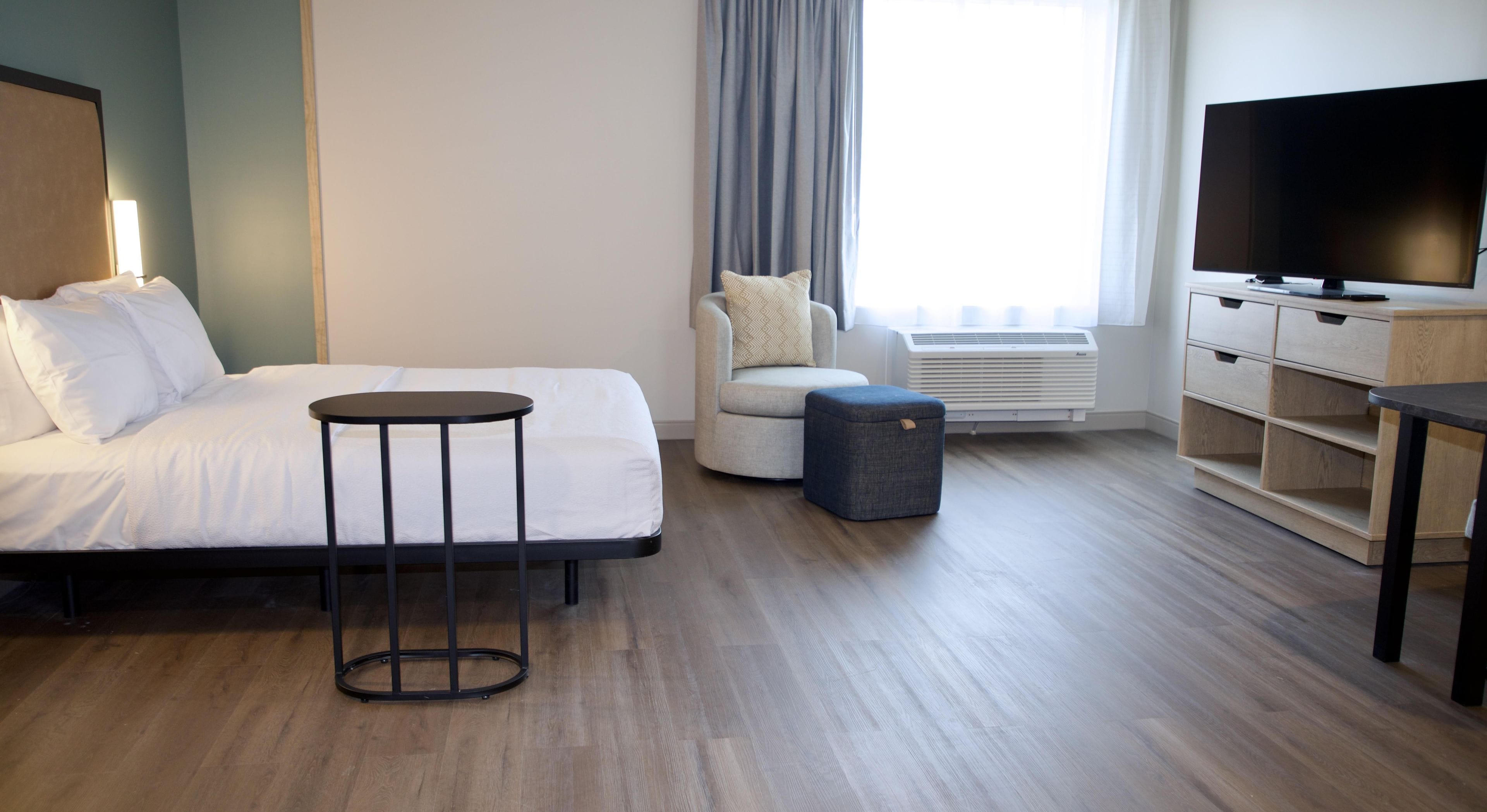 Una habitación de hotel con cama, una mesita redonda pequeña, una silla, un televisor y un armario.
